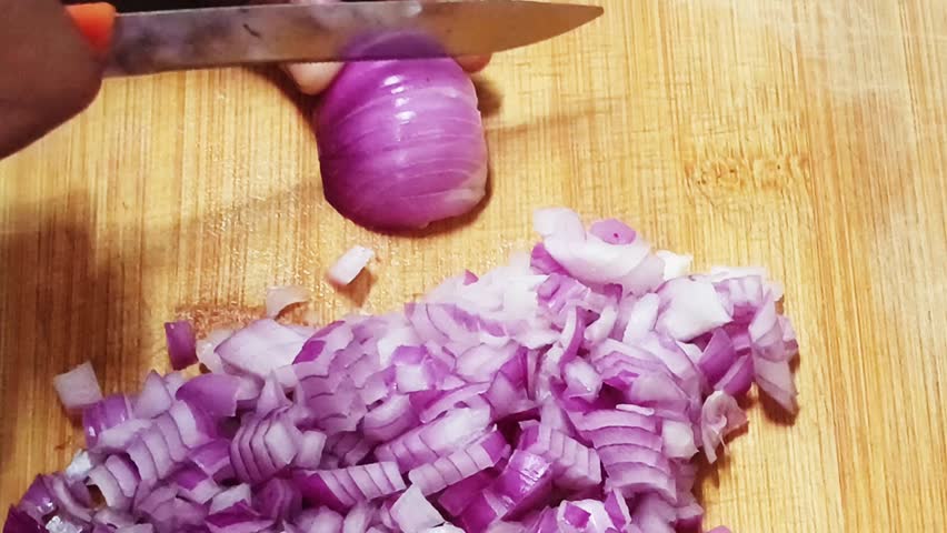 Close-up of hands chopping a red onion on a wooden board. Useful for cooking tutorials, recipe visuals, kitchen preparation and healthy food content.