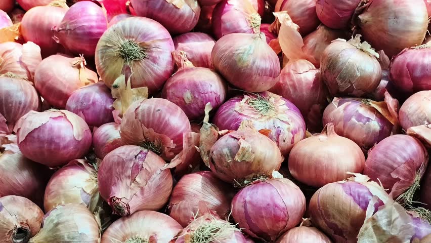 A close-up view of fresh red onions stacked in bulk at a local market. Great for agriculture, organic produce, kitchen ingredients, food backgrounds and vegetarian cooking themes.
