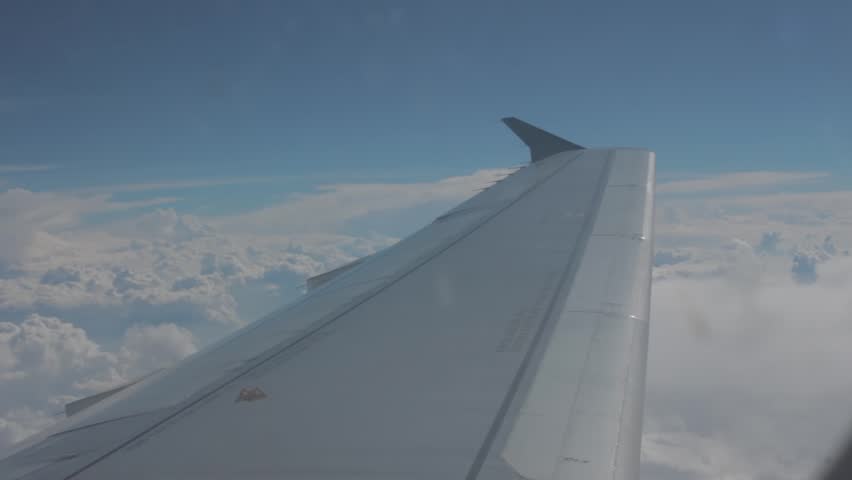 View of airplane wing above clouds under clear blue sky