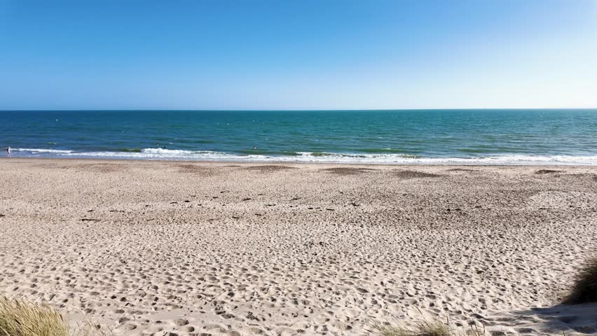Warm summer seaside beach views of the sand and sea, waves gently rolling in on a beach in Dorset, England, United Kingdom