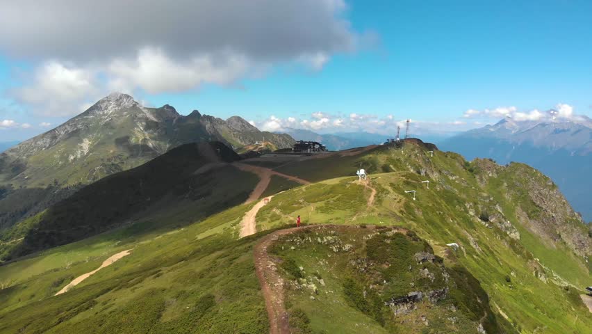 Beautiful mountain landscape. High-mountain massif, clouds over mountain peaks. Traveler goes to the top of the mountain, the figure of a man in red, aerial video shooting .