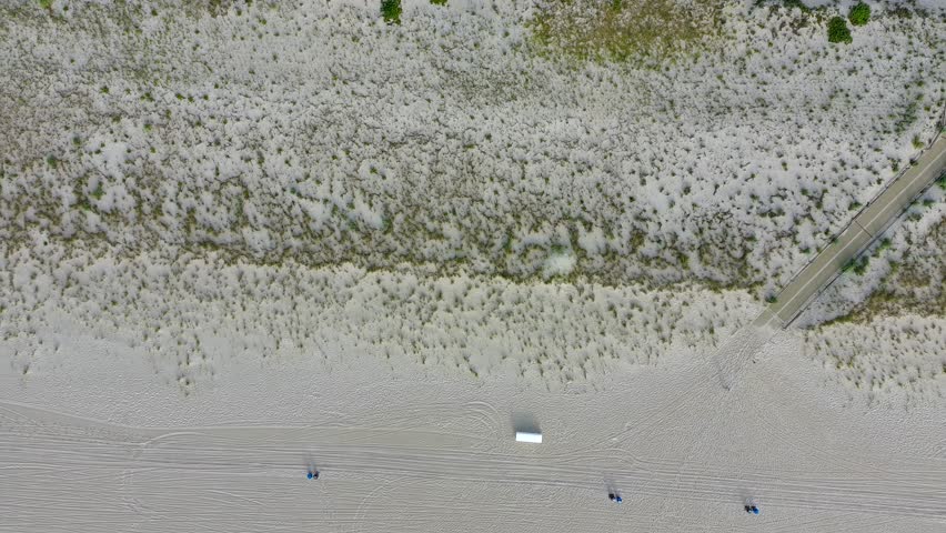 A beach with a road running along it. The road is empty and the beach is covered in sand