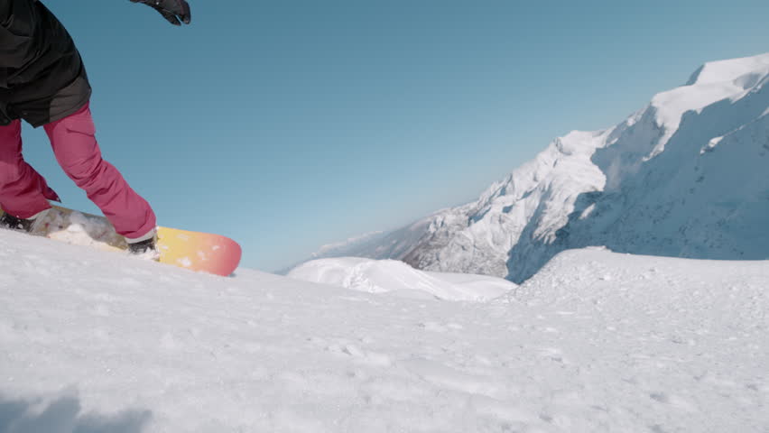 SLOW MOTION, CLOSE UP: Female snowboarder tumbles into soft snow on a sunny alpine slope as she tries to learn to carve on a snowboard. Snow flies toward the camera while she crashes with a smile.