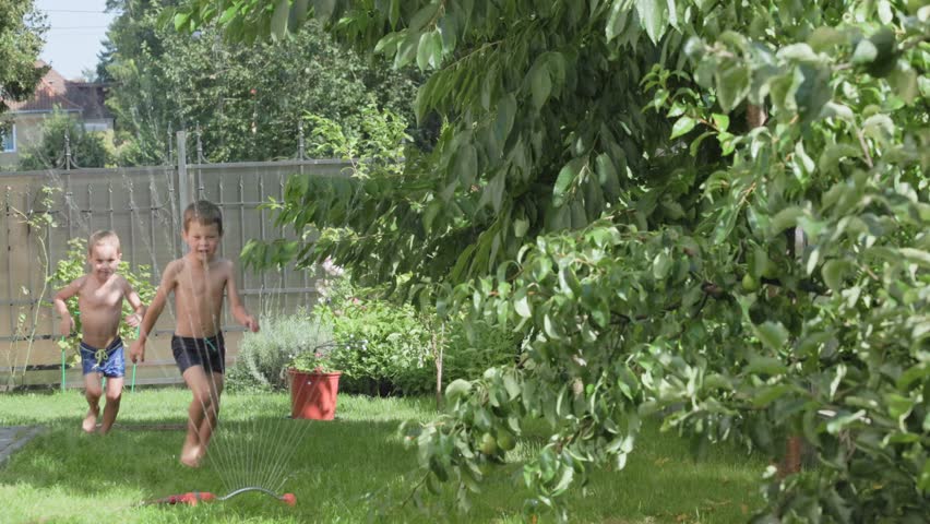 Two joyful children are happily playing outside in a sunny garden filled with exciting water activities