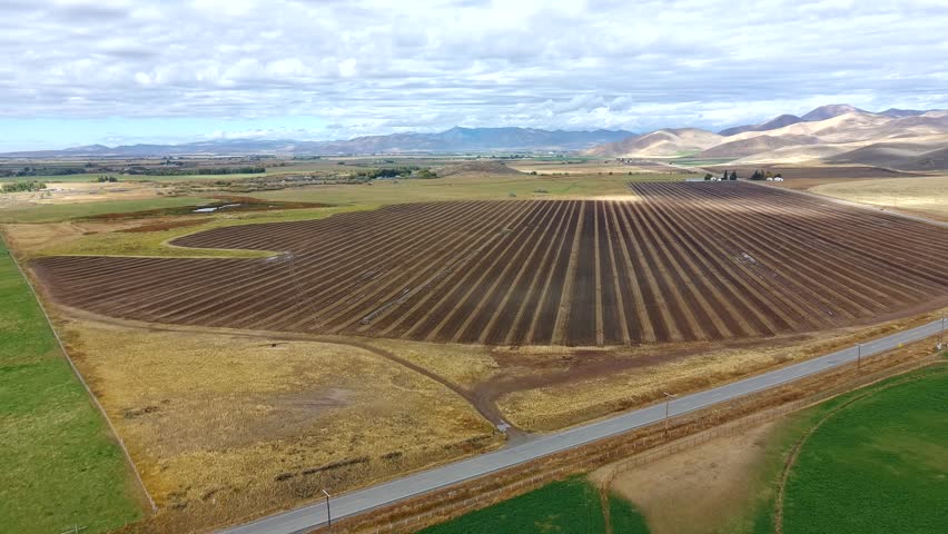 A large field with a road running through it. The sky is cloudy and the sun is shining