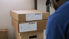 Over-shoulder shot of African American male warehouse employee using handheld infrared scanner device to read information in barcodes on packages while processing boxes for delivery - Powered by Shutterstock - Get 15% off with code: PIKWIZARD15
