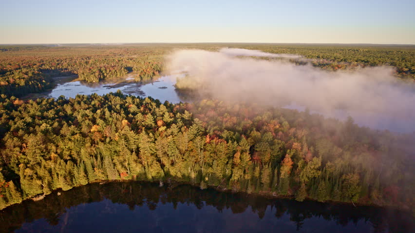 Drone flies above water as sunrise mist begins to rise.