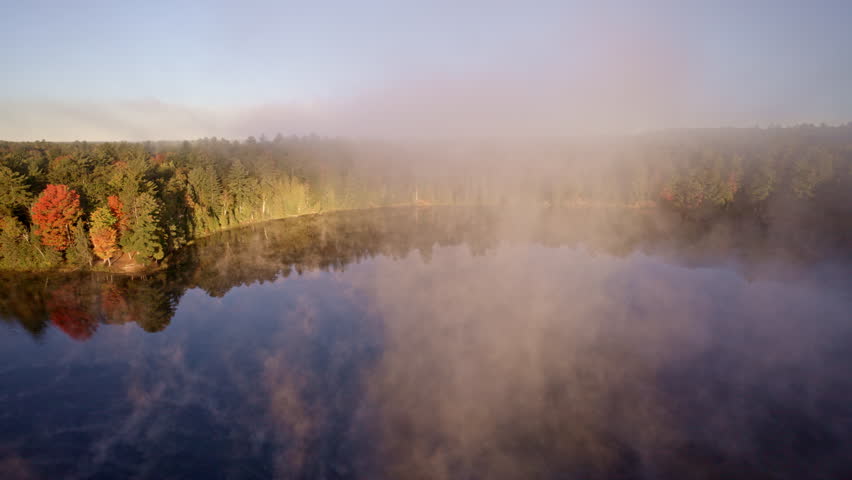 Drone glides over water as morning mist rises into the air.