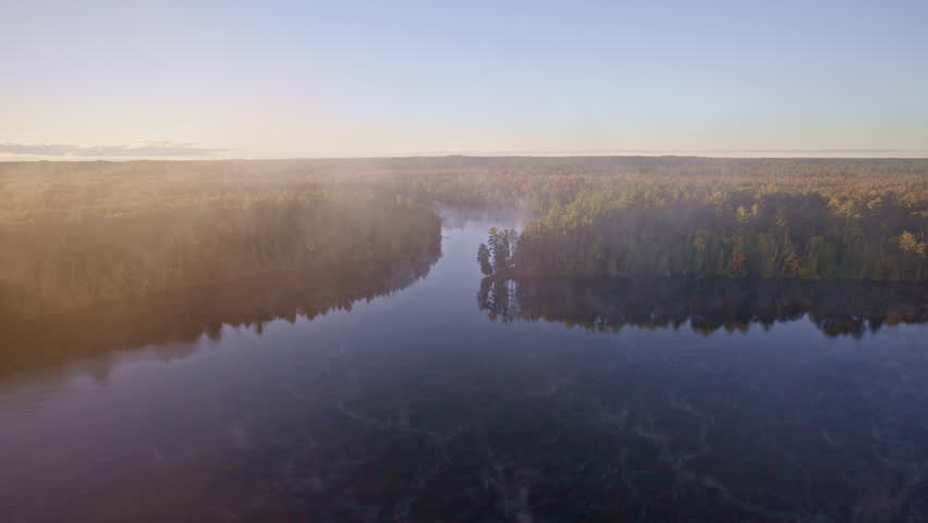 Drone sweeping shot of dawn mist floating upward over water.