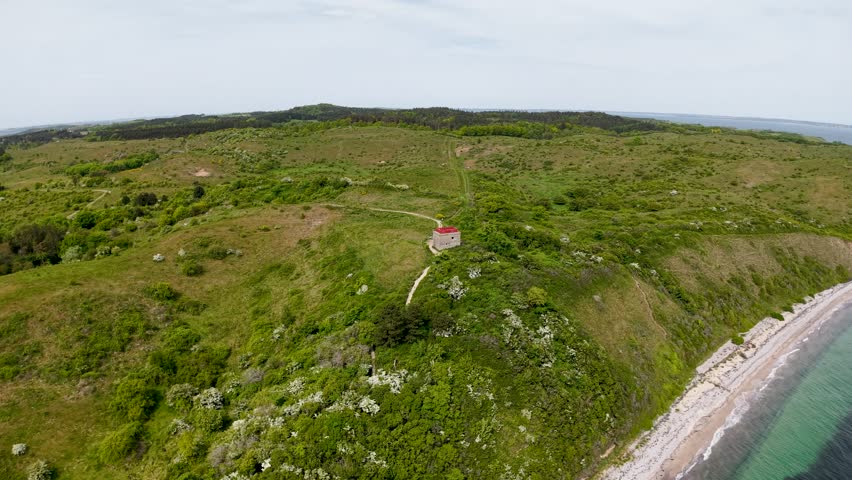 Drone footage captures a lush green bluff along the Danish coast overlooking a calm sea. The aerial view highlights the rugged coastline, vegetation, and peaceful atmosphere.