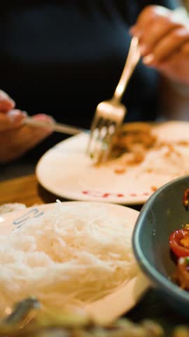 Person enjoys spicy som tam papaya salad with noodles in warmly lit Bangkok dining setting