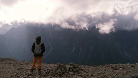 Wide shot of a hiker with a small backpack standing on a rocky ridge facing the cloud-covered Hotaka mountains under a dramatic sky. - Powered by Shutterstock - Get 15% off with code: PIKWIZARD15