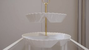 White glossy ceramic and gold metal tiered serving dish is set down on a glass surface. A light, delicate clink rings out. - Powered by Shutterstock - Get 15% off with code: PIKWIZARD15