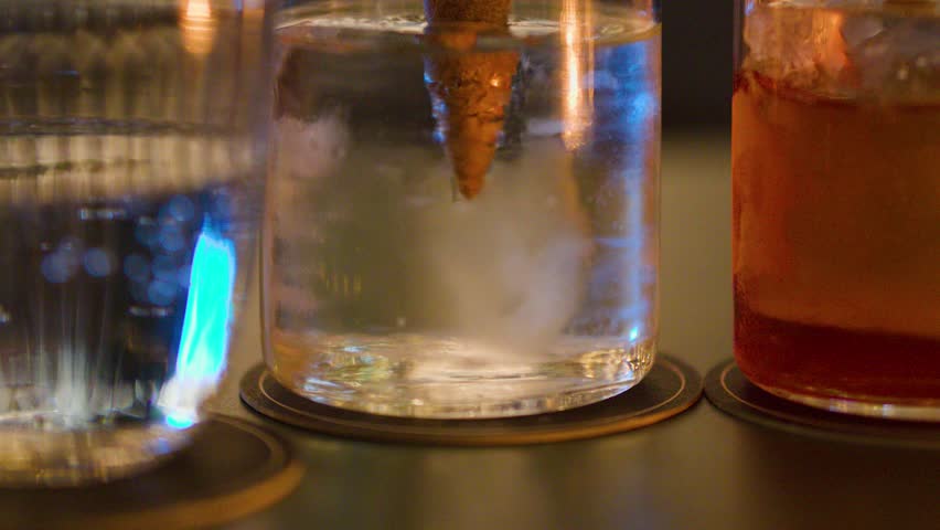 Ice cream cone garnish slowly lowered into clear cocktail glass, evening bar lighting, shallow focus