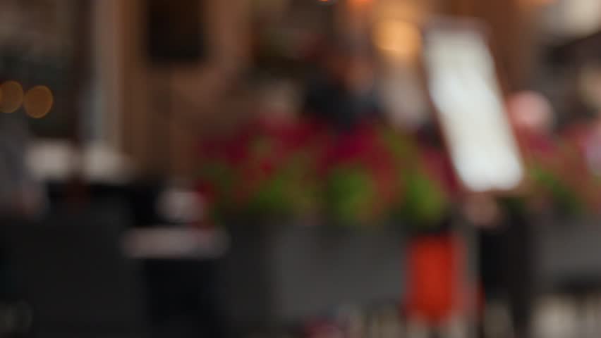 Camera focuses from blurred street scene to sharp red cocktail glass, evening outdoor cafÃ© ambiance