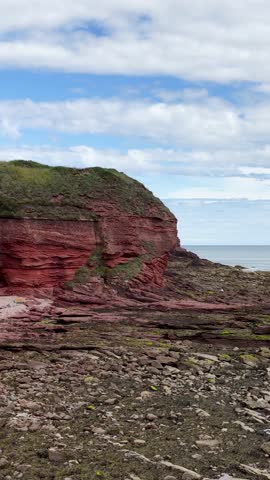 Camera pans across red sandstone cliffs, rocky shoreline, and North Sea under daylight skies