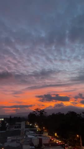 Dramatic sunset sky with glowing orange and purple clouds over a city landscape and distant mountains, peaceful evening light and warm atmospheric view.