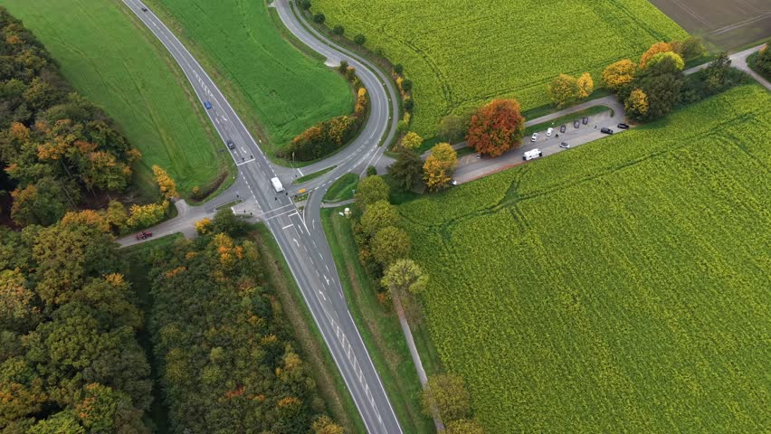 Rural American road intersection surrounded by green fields and vibrant autumn foliage, with cars parked along a countryside lane during fall season. aerial top down shot. Traffic scene suburbia.