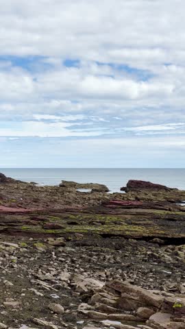 Camera slowly pans over layered red sandstone cliffs, rocky shoreline, and North Sea under daylight