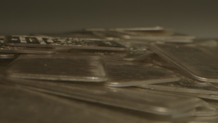 Extreme close up of a pile of 1 gram silver bars and a hand collecting a bunch of precious metal plates