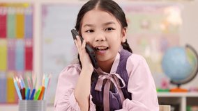 Smiling schoolgirl interacts with smartphone at desk, colorful classroom background, bright natural lighting - Powered by Shutterstock - Get 15% off with code: PIKWIZARD15