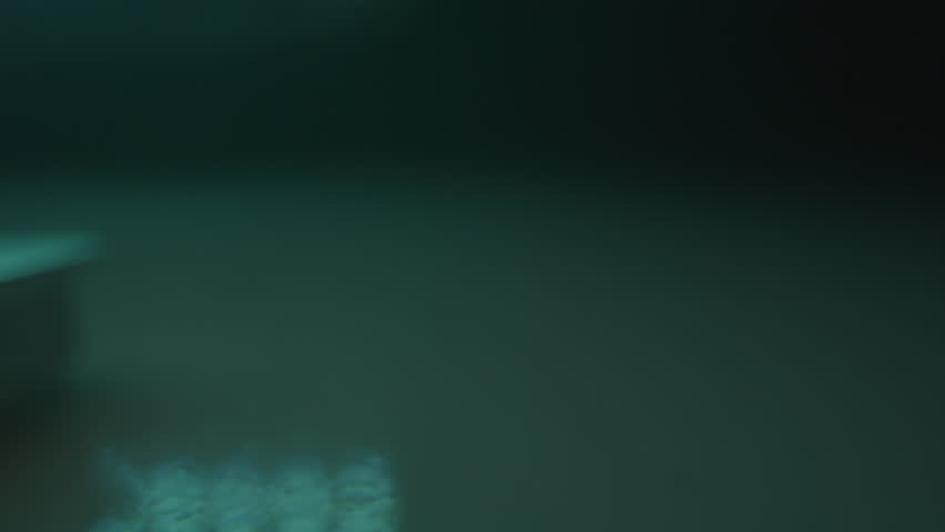 Beautiful dolly of stacks of silver bars in a smoke filled blue room. The camera moves over the precious metal in a surrealistic vault.