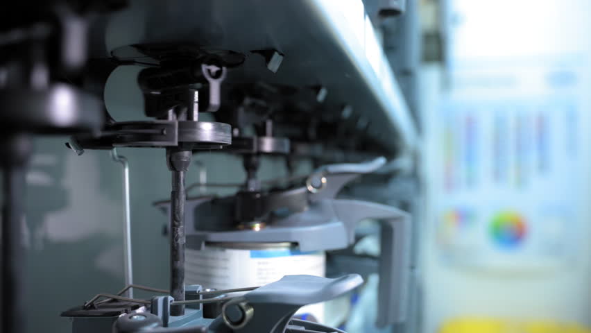 Close-up of an industrial paint mixing machine. Mechanical arms and nozzles dispense and blend paint inside a container, showing the automated mixing process.