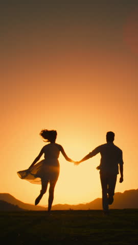 Silhouette of Happy Couple Running Hand in Hand into Sunset. Vertical Video