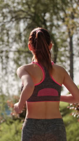 fit woman jogging in park morning sunlight vertical slow motion view from back healthy lifestyle energy motivation freedom wellness movement balance inspiration