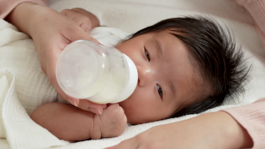 Mother hands feeding milk bottle to her baby.