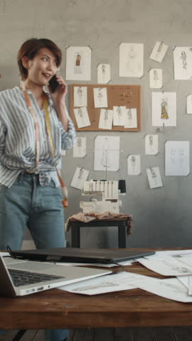 energetic female fashion designer discussing creative ideas by phone in atelier symbol of enthusiasm innovation sustainable mindset vertical slow motion fullhd stock video