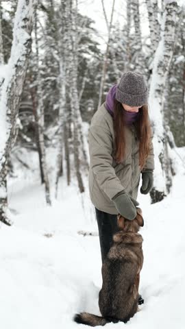A young woman relaxes during a walk in a winter forest with her dog.
