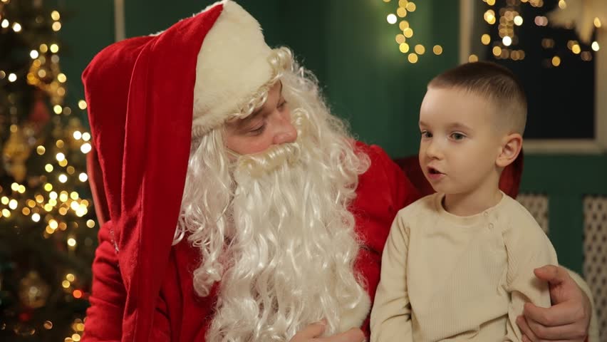 Santa Claus listens attentively to a young boy while sitting together in a warm, festive Christmas setting decorated