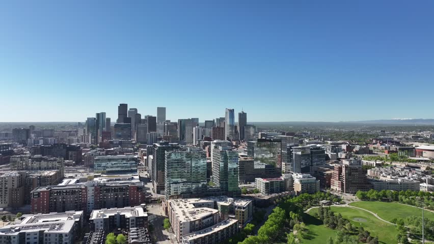 Aerial view of downtown Denver showing modern high rise buildings under a clear blue sky, drone flying sideways over commons park