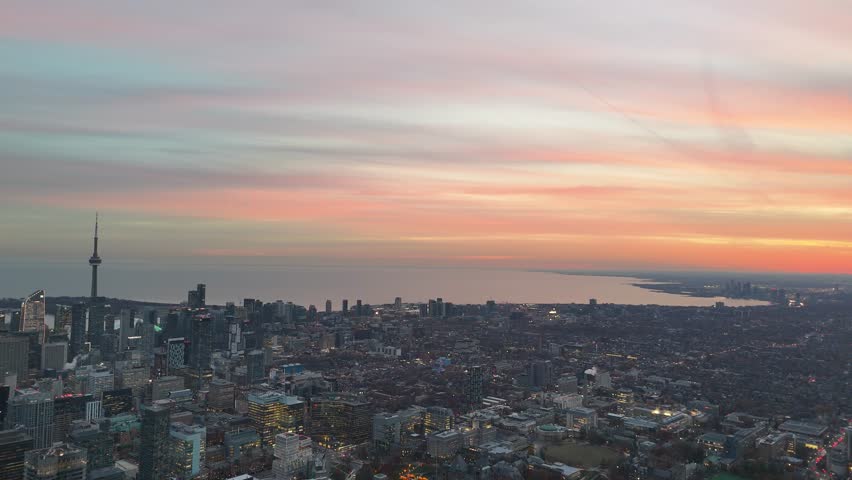Slow-motion drone footage captured during sunset, flying left across the vibrant Toronto skyline and the iconic CN Tower, looking out over Lake Ontario
