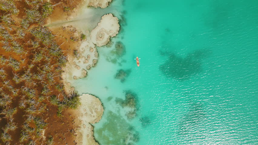 Drone view of couple kayaking on Bacalar Lagoon by turquoise waters and unique stromatolite formations in Mexico