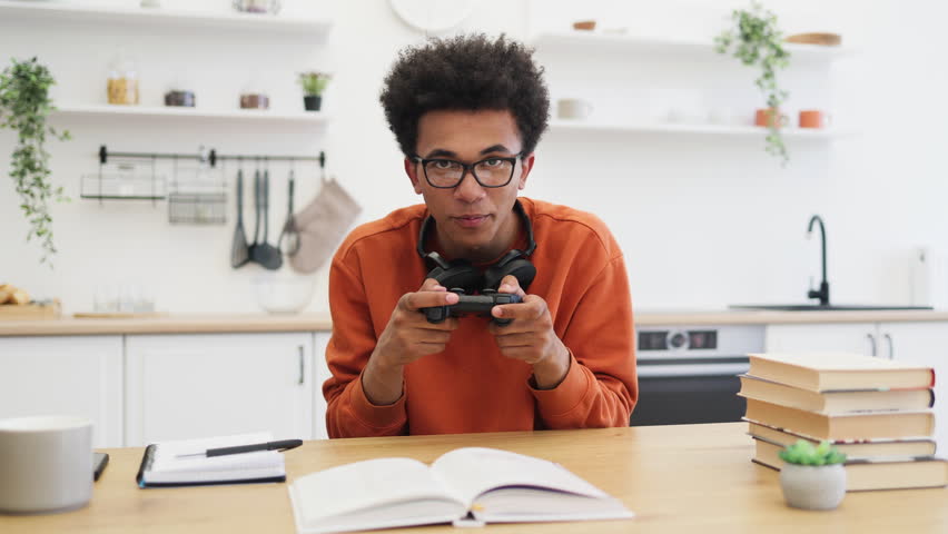 A young man with glasses celebrates a win while holding a game controller, showing excitement in a home setting.