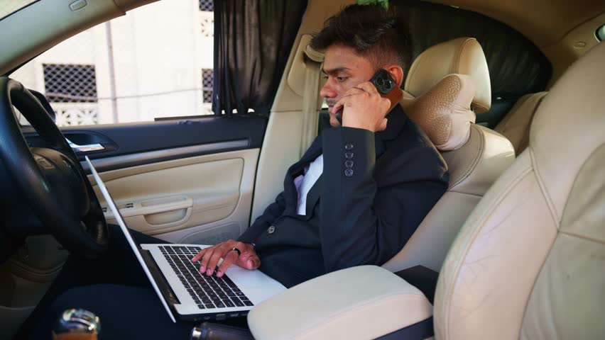 Businessman in Suit Using Laptop and Phone Inside Car, Young Executive Manages Work Remotely from Vehicle, Entrepreneur Multitasks Uses Tech Gadgets into Motorcar, Staff Balances his job via device