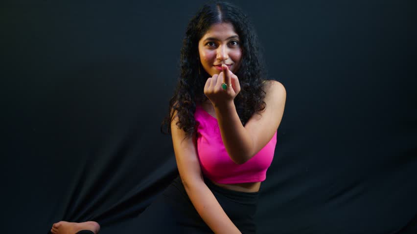 Curly haired woman strikes bold pose under bright lights, Classy Female flaunts pink crop top in studio, Fashionable shows glam outfit through grace, Stylish Lady delivers posture with seductive charm