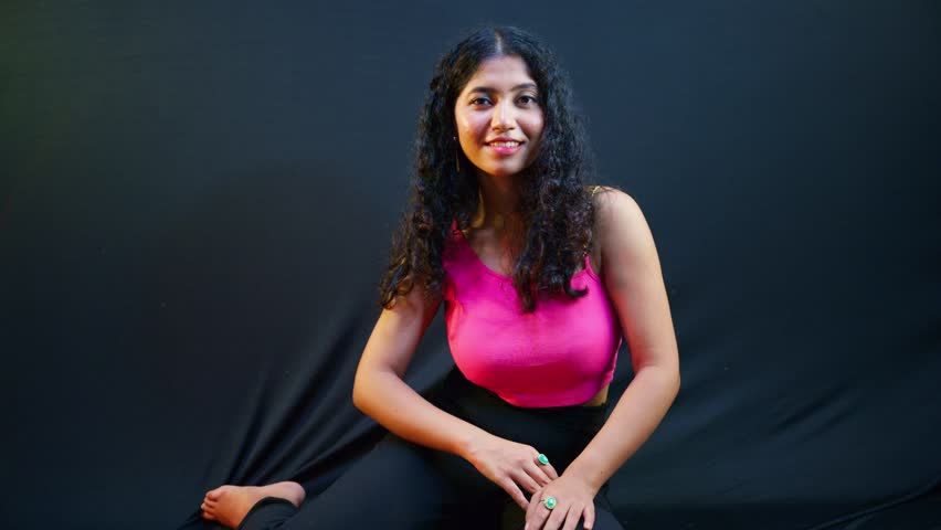 Classy Female flaunts pink crop top in studio, Curly haired woman strikes bold pose under bright lights, Fashionable shows glam outfit through grace, Stylish Lady delivers posture with seductive charm