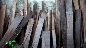 A pile of rough, dark, used wooden planks, leaning against a dull concrete wall, looks wet and shiny from the rain. - Powered by Shutterstock - Get 15% off with code: PIKWIZARD15