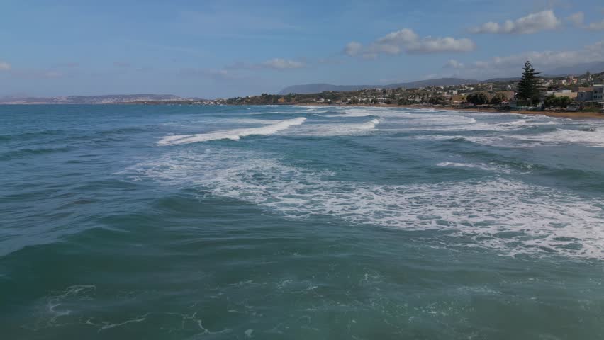 Aerial, panoramic view of the northern coast of the island of Crete. Waves crashing against the rocky pier near the town of Agia Marina and Platanias, Crete, Greece