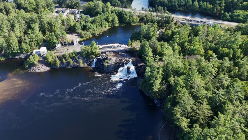 A mesmerizing aerial view of High Falls on the Muskoka River in Bracebridge, Ontario, Canada showing powerful cascading water surrounded by lush green forest.