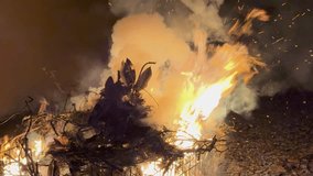 Large bonfire consuming a pile of dry branches and an effigy during a nighttime celebration. Intense orange flames. Billowing smoke. And flying embers illuminate the dark sky in a captivating display - Powered by Shutterstock - Get 15% off with code: PIKWIZARD15
