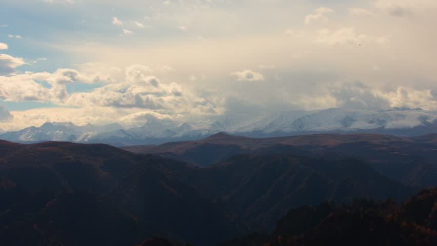 A panoramic view of mountains under a cloudy sky. The landscape features rugged peaks and valleys, showcasing natural beauty and tranquility.