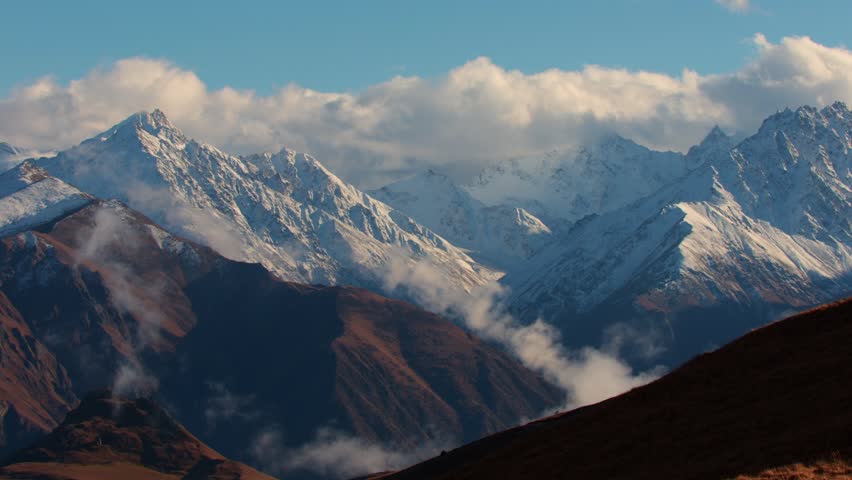 Snow-capped mountains under a blue sky with clouds. The landscape features rugged peaks and valleys, showcasing natural beauty and tranquility.
