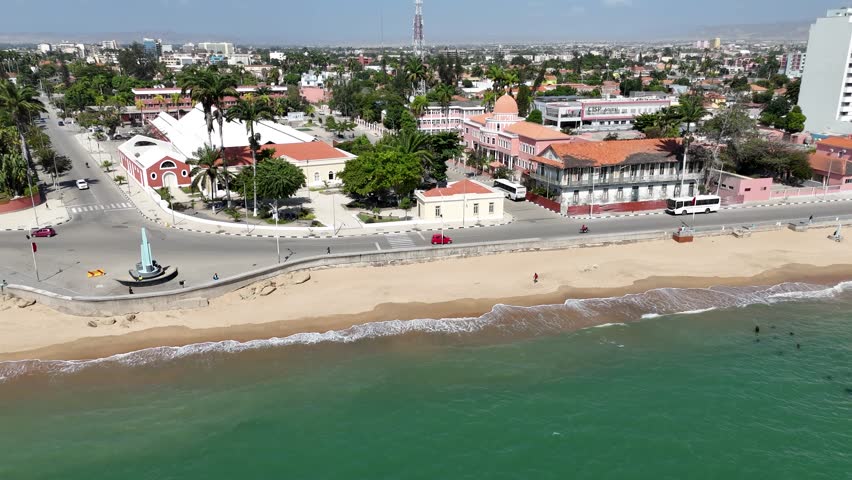Aerial view of Benguela, Angola, showing coastal neighborhood with sandy beach, ocean waves, and colorful seaside buildings in tropical sunlight