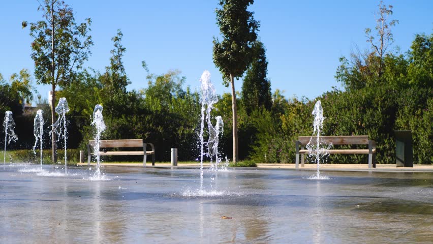 Slow-motion video of water fountains in city park under warm summer sunlight, creating lively, refreshing and joyful urban atmosphere. Perfect for outdoor leisure, tourism and lifestyle content