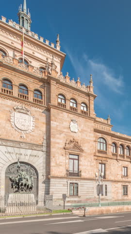 Panorama showing Cavalry Academy facade timelapse in Plaza de Zorrilla, Valladolid, Spain. Historic military building with intricate architecture, surrounded by busy urban scene under blue cloudy sky