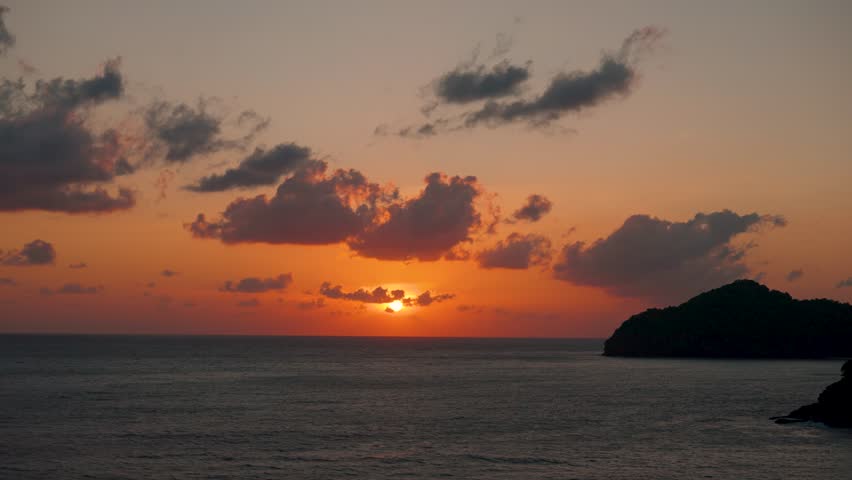 4K Landscape shot of sunset with orange clouds above the sea water as seen from Langkawi island in Malaysia. Scenic view of sunset above the Andaman sea. Orange clouds and sun above sea water. 